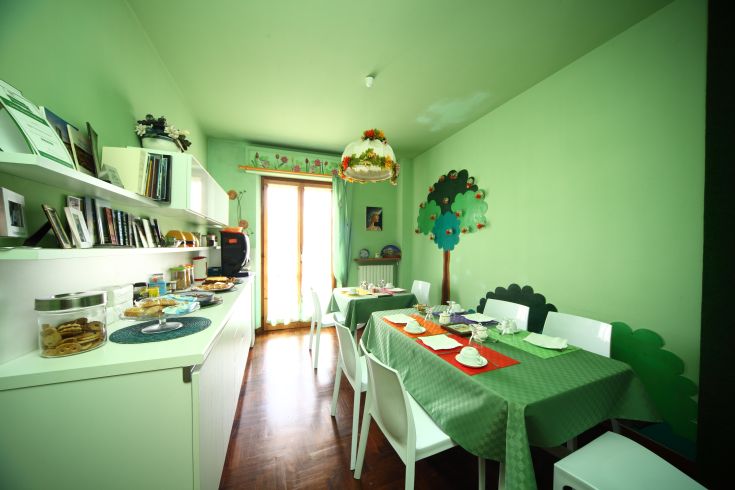 Ein einfacher und lebhafter Frühstücksraum im B&B, mit grünen Dekorationen und für die Gäste gedeckten Tischen.