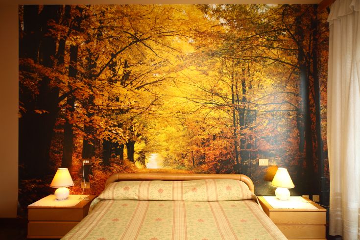 Ein einfacher Raum mit einer dekorierten Wand, die eine herbstliche Waldlandschaft darstellt.