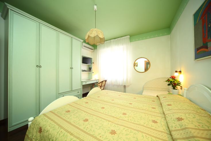 Ein einfaches und komfortables Zimmer mit Schrank, Schreibtisch und beruhigenden Grüntönen für Entspannung.