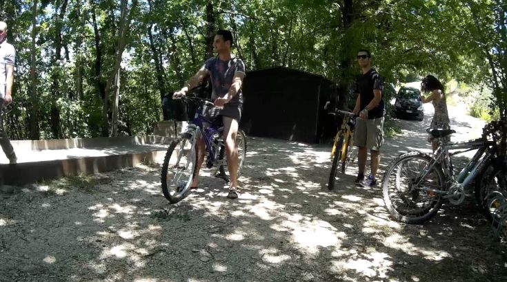 Un gruppo di persone in bicicletta si prepara a partire in un'area boschiva illuminata dal sole.