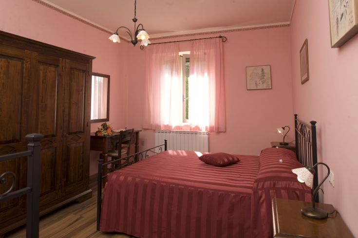 Camera accogliente con tonalità rosa e arredo in legno, ideale per un soggiorno rilassato.