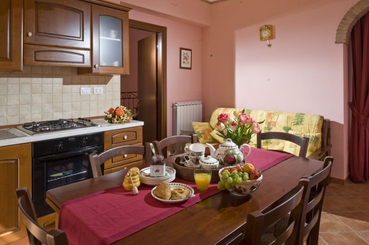 Una cucina semplice e ben illuminata, dotata di un tavolo preparato per la colazione con vari cibi colorati.