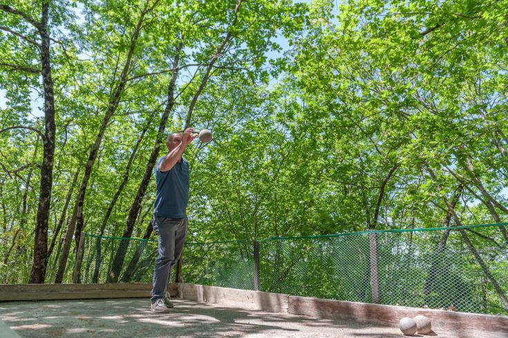 Un uomo si dedica al gioco delle bocce in un campo verde, circondato da alberi e un ambiente naturale.