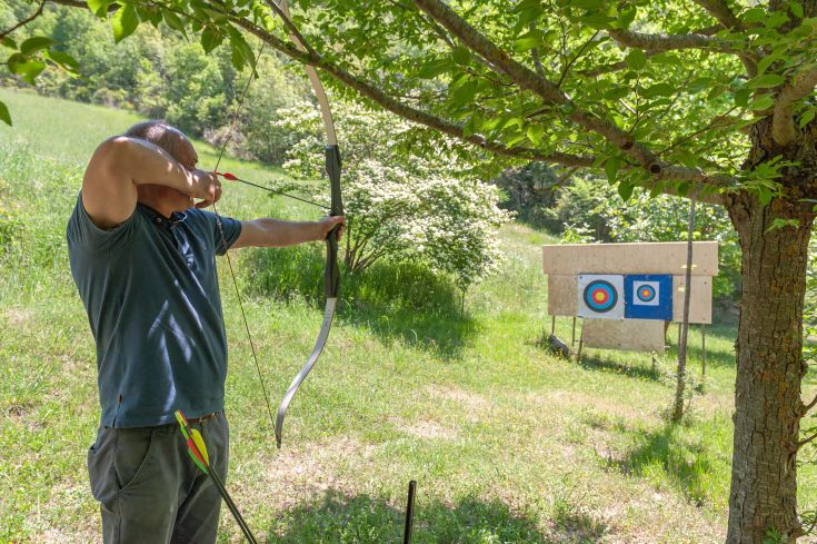 Un arciere si prepara a colpire il bersaglio nel verde, tra gli alberi e la tranquillità della natura.
