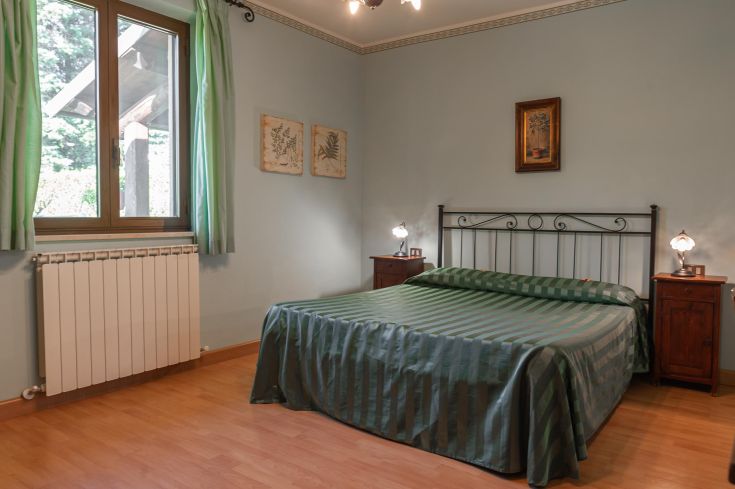 Camera accogliente con letto matrimoniale, finestre e dettagli decorativi in tonalità verdi.
