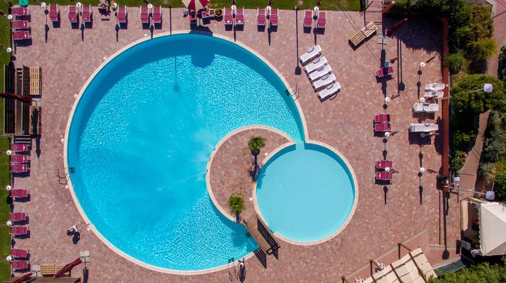 Panorama di una piscina circolare immersa nel verde, dotata di lettini e ombrelloni.