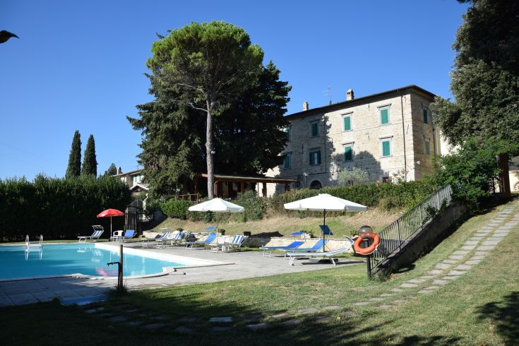 Well-maintained garden with a pool next to an ancient building, set in a hilly landscape.