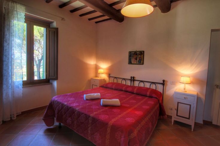 Cozy bedroom with a view of the Umbrian hills, furnished in warm tones and illuminated by natural light.