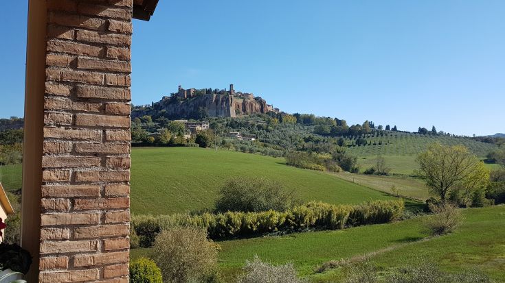Scena sulla campagna umbra con la Rupe di Orvieto sullo sfondo, mentre un B&B è visibile in primo piano.
