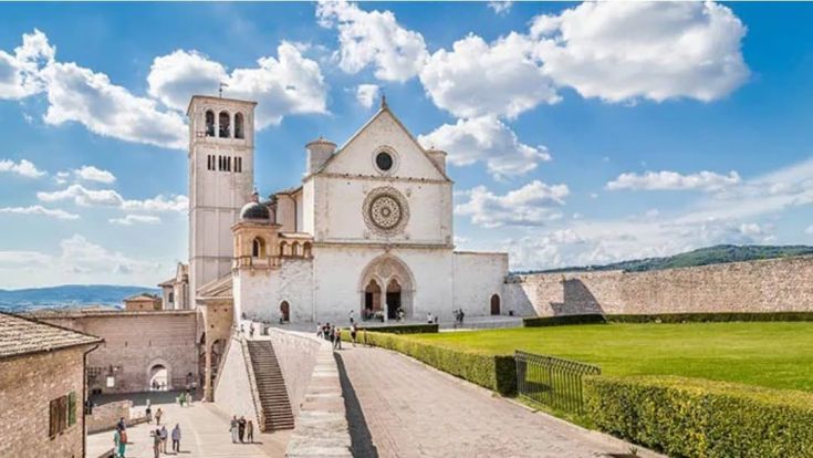 La Basilique de San Francesco à Assise sous un ciel bleu avec quelques nuages blancs.