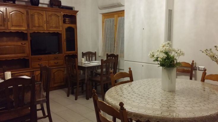 Salon simple avec des meubles en bois, une table ronde et des décorations florales sur les meubles.