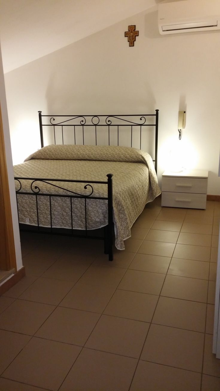 Une chambre simple avec un lit double, caractérisée par des meubles essentiels et une lumière chaude pour une atmosphère relaxante.