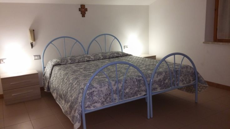 Chambre double accueillante avec un lit bleu, décoration minimaliste et éclairage doux.