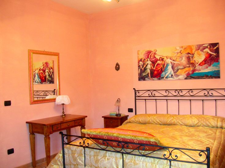 Ein Schlafzimmer mit schlichten Dekorationen, rosa Wänden, einem Spiegel und einem Bild über dem Bett.