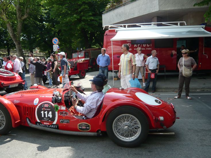 Ein roter Vintage-Sportwagen steht geparkt, während Leute ihn neugierig beobachten.
