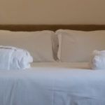 Ein geräumiges Doppelbett mit weißen Bettlaken und ordentlich gefalteten, weichen Handtüchern.