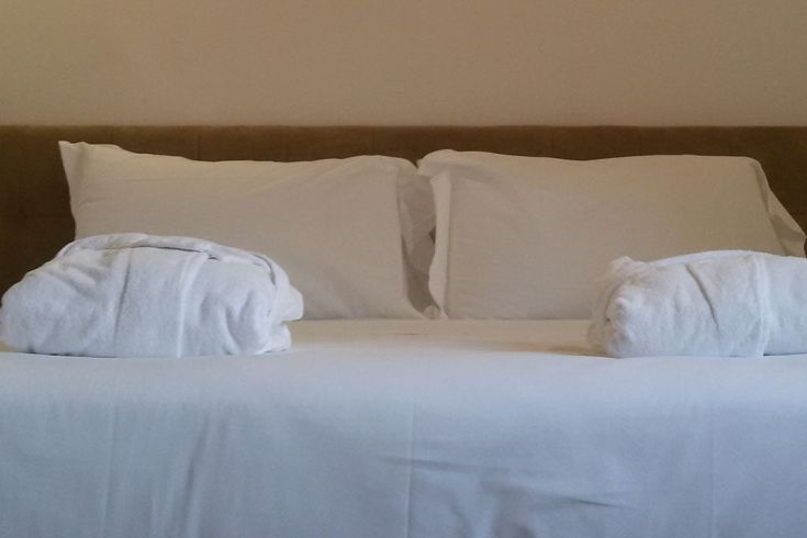 Ein einfaches, bequemes Bett mit weißen Kissen und gerollten Handtüchern, bereit, Gäste zu empfangen.