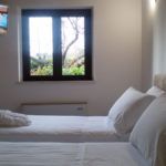 Ein einfaches Zimmer mit zwei Einzelbetten und einem großen Fenster mit Blick auf einen Garten.