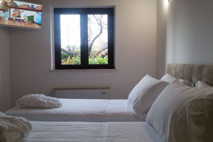 Ein geräumiges und gut beleuchtetes Schlafzimmer mit zwei Betten, das auf einen gepflegten Garten blickt.