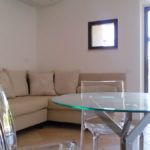 Ein modernes Wohnzimmer mit einem hellen Sofa und einem Glastisch, schlicht eingerichtet.