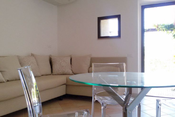 Ein einfacher Lounge-Bereich mit Sofa und Glastisch, beleuchtet von natürlichem Licht.