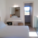 Helle Zimmer mit einfacher Einrichtung und einem Fenster mit Blick auf die umliegende Natur.