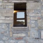 Ein Fenster, das in einer Steinmauer eingelassen ist, mit einem einfachen und rustikalen Design.