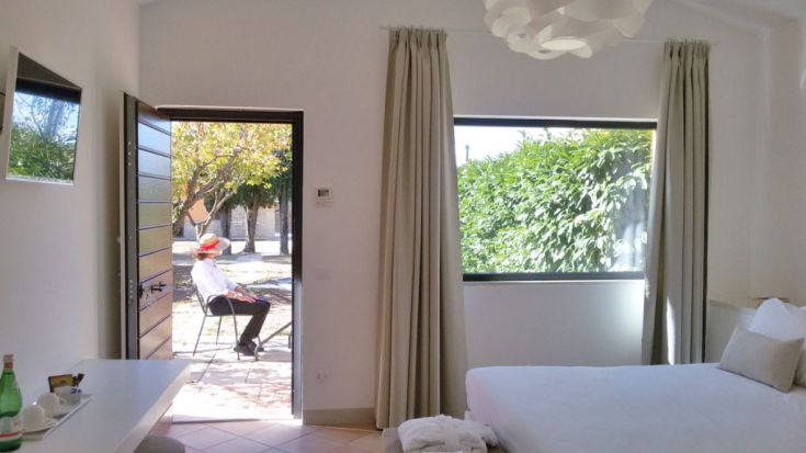 Ein helles Zimmer mit Zugang zu einem Garten, ein Mann sitzt draußen, um die Sonne zu genießen.