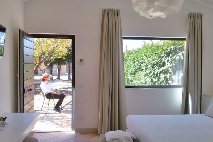 Ein gut beleuchtetes Zimmer mit Blick auf einen Garten. Ein Mann sitzt im Garten.