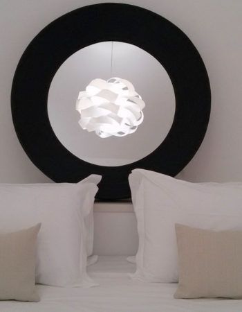 Eine einfache Einrichtung mit einem großen runden Spiegel und einer Lampe über dem Bett.