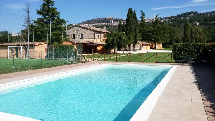 Ein Pool im Zentrum einer Landschaft, umgeben von schöner grüner Fläche und einem rustikalen Haus.
