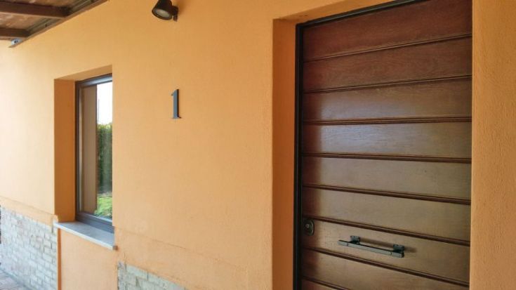 Eingang eines Gebäudes mit orangefarbenen Wänden und einer Holztür in einer friedlichen Umgebung.