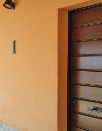 Eingangstür eines Gebäudes in orangenen Farbtönen, mit der Nummer 1 sichtbar auf der Tür.
