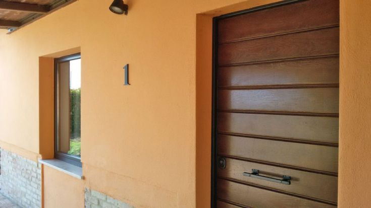 Eingang eines Hauses mit einer Holztür und der Hausnummer 1 an einer orangefarbenen Wand.