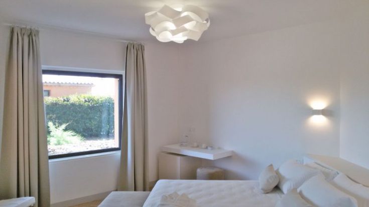 Ein einfaches Zimmer mit sanfter Beleuchtung, das auf einen Garten blickt.