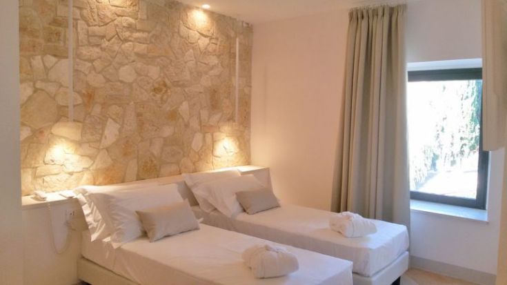 Helle Zimmer mit einer Steinwand und zwei einfach angeordneten Einzelbetten.