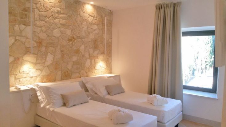 Ein einfaches Zimmer mit einer Steinmauer und Einzelbetten, gut beleuchtet durch natürliches Licht.