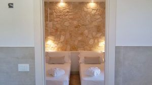 Gemütliches Zimmer mit Einzelbetten, warmer Beleuchtung und Steinwand. Intime und entspannende Atmosphäre.