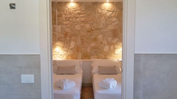 Zimmer mit Steinenwand und Einzelbetten, in einem schlichten und einladenden Stil.