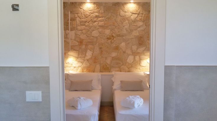 Innenansicht eines Zimmers mit Steinwand und weißen Betten, ideal für einen ruhigen Aufenthalt.