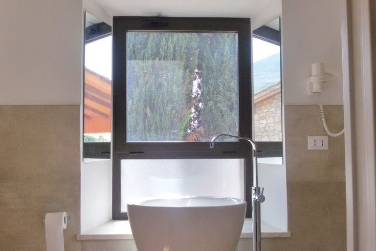 Ein modernes Badezimmer mit großen Fenstern, die einen Blick auf eine natürliche Landschaft bieten, ausgestattet mit einem einfachen Waschbecken.