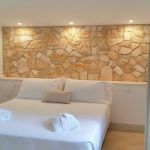 Ein einfaches Zimmer mit hellen Steinwänden und weißen Betten, beleuchtet von modernen Lampen.