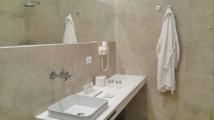 Ein modernes und gut eingerichtetes Badezimmer mit einem weißen Waschbecken und einem Bademantel, der am Schrank hängt.