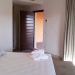 Ein aufgeräumtes Zimmer mit einer offenen Tür. Das Bett ist gemacht und die Handtücher sind ordentlich gefaltet.