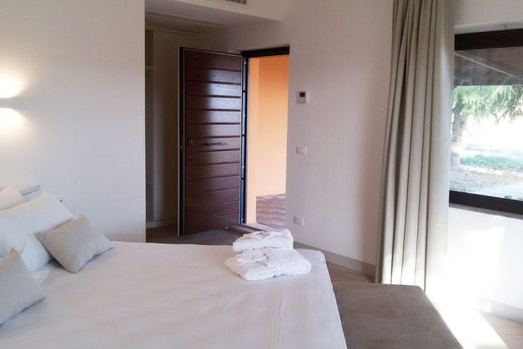 Einfaches und elegantes Zimmer mit offener Tür, hellen Vorhängen und einem schlichten Bett.