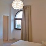 Ein helles und einladendes Zimmer mit einem Bett, einem Vorhang und einem modernen Kronleuchter.