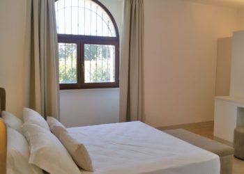 Ein helles und gemütliches Zimmer mit einem Doppelbett und einem großen Fenster im Bogen.