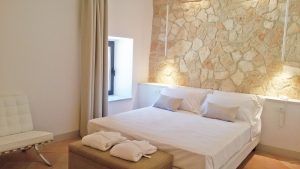 Einfaches Schlafzimmer mit Doppelbett, Steinwand und zeitgenössischen Möbeln.