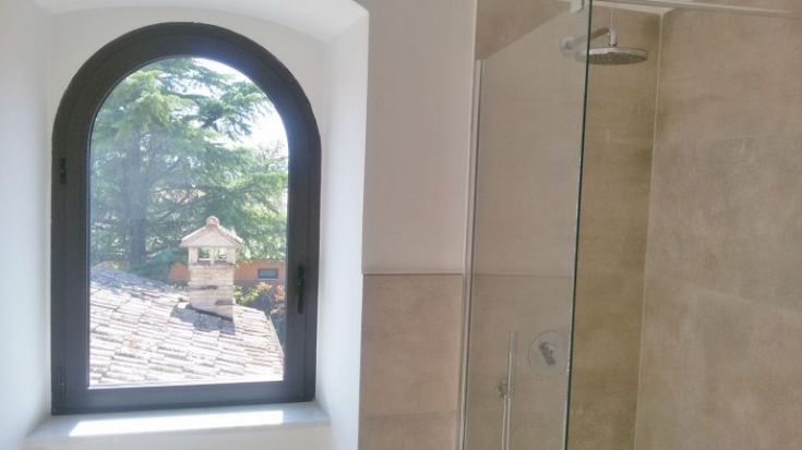 Eine Szene in einem modernen Badezimmer mit einer transparenten Dusche, die auf eine natürliche Außenszene blickt.