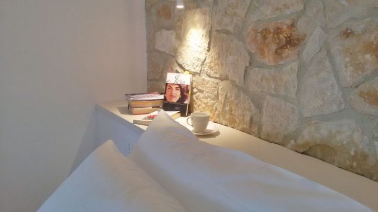 Eine einfache und gemütliche Leseecke mit Büchern und einer Tasse auf einem kleinen Tisch neben einer Steinmauer.